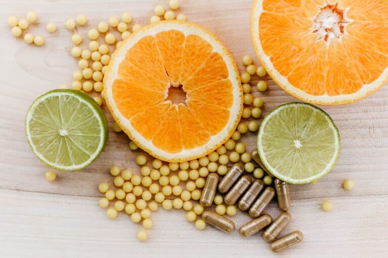 Fresh citrus fruits including orange and lime slices with dietary supplements and herbal capsules on a wooden surface. Perfect for promoting immune health, vitamin C, and natural wellness.