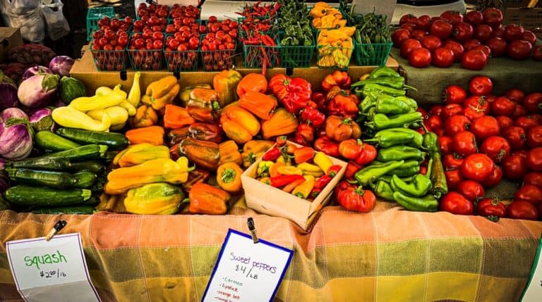 Fresh colorful bell peppers, tomatoes, zucchini, and squash at a local farmers market, showcasing healthy produce options with vibrant display for outdoor shopping.