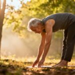 Gentle elderly woman practicing outdoor stretching in the woods during sunrise for improved flexibility and relaxation.