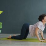 Gentle woman practicing yoga on a green mat in a modern, minimalistic room for stretching and flexibility exercises.