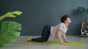 Gentle woman practicing yoga on a green mat in a modern, minimalistic room for stretching and flexibility exercises.