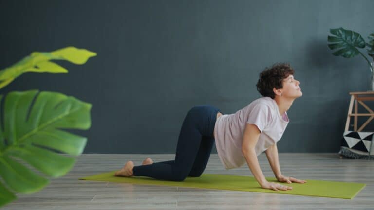 Gentle woman practicing yoga on a green mat in a modern, minimalistic room for stretching and flexibility exercises.