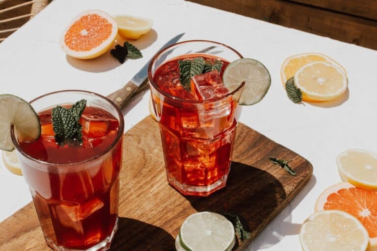 Refreshing iced hibiscus tea with lime slices, garnished with fresh mint leaves, served on a wooden board with citrus fruits and slices, perfect for healthy hydration and relaxation.