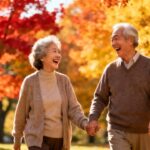 Joyful elderly couple walking outdoors in autumn park, holding hands, smiling, vibrant fall foliage, healthy aging, outdoor stretching routines, wellness, happiness, senior fitness, fall season activities.